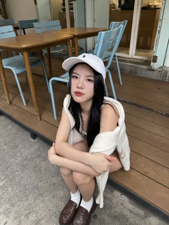 Pang Sabsima Payakharn đội mũ trắng ngồi trước quán cà phê
